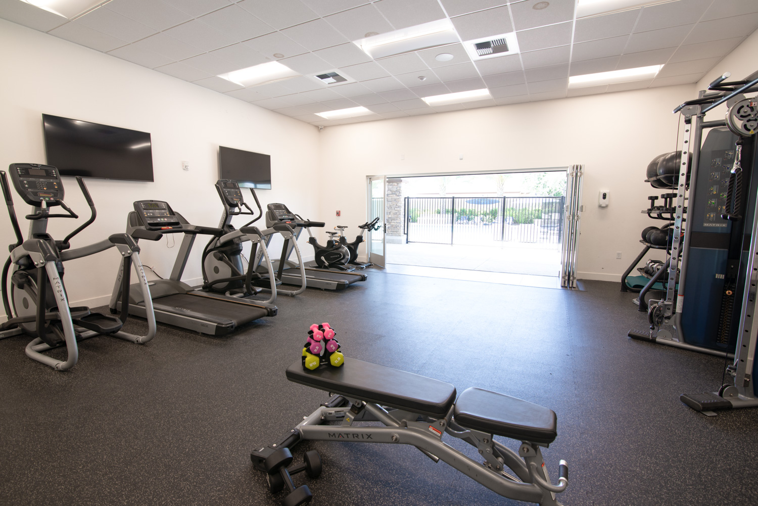 Before image of a high-end fitness center equipped with top-notch workout machines. Although the space is designed for an optimal exercise experience, the photo's colors are not accurately represented, and the view from the expansive window wall is obscured, diminishing the visual appeal of the setting.