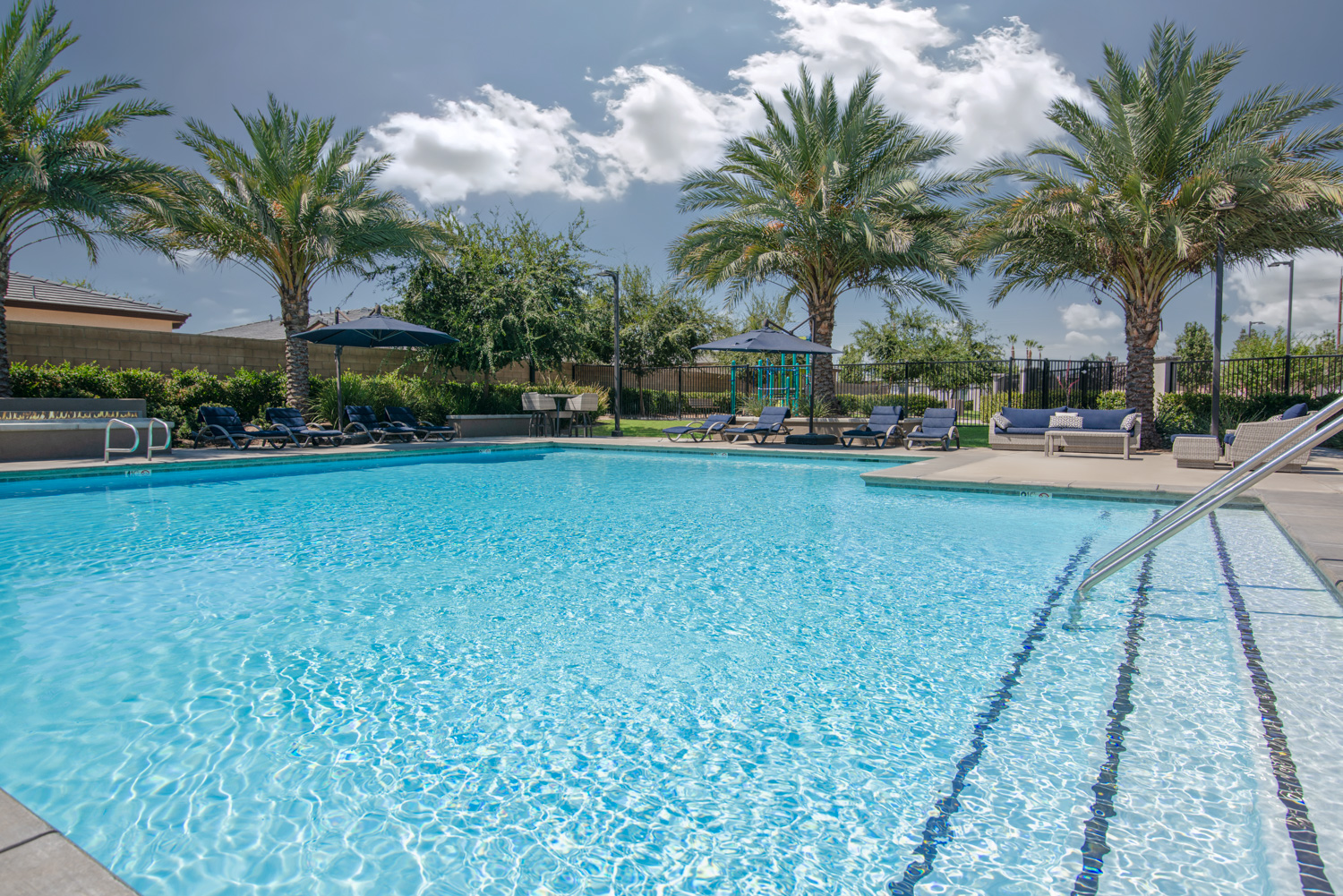 Enhanced after image of a pool area, showcasing a vibrant, sparkling blue pool and meticulously detailed landscaping. The concrete flaws have been corrected, and the overall setting is complemented by a dramatic yet believable sky, creating an ideal visual representation of an inviting outdoor space.